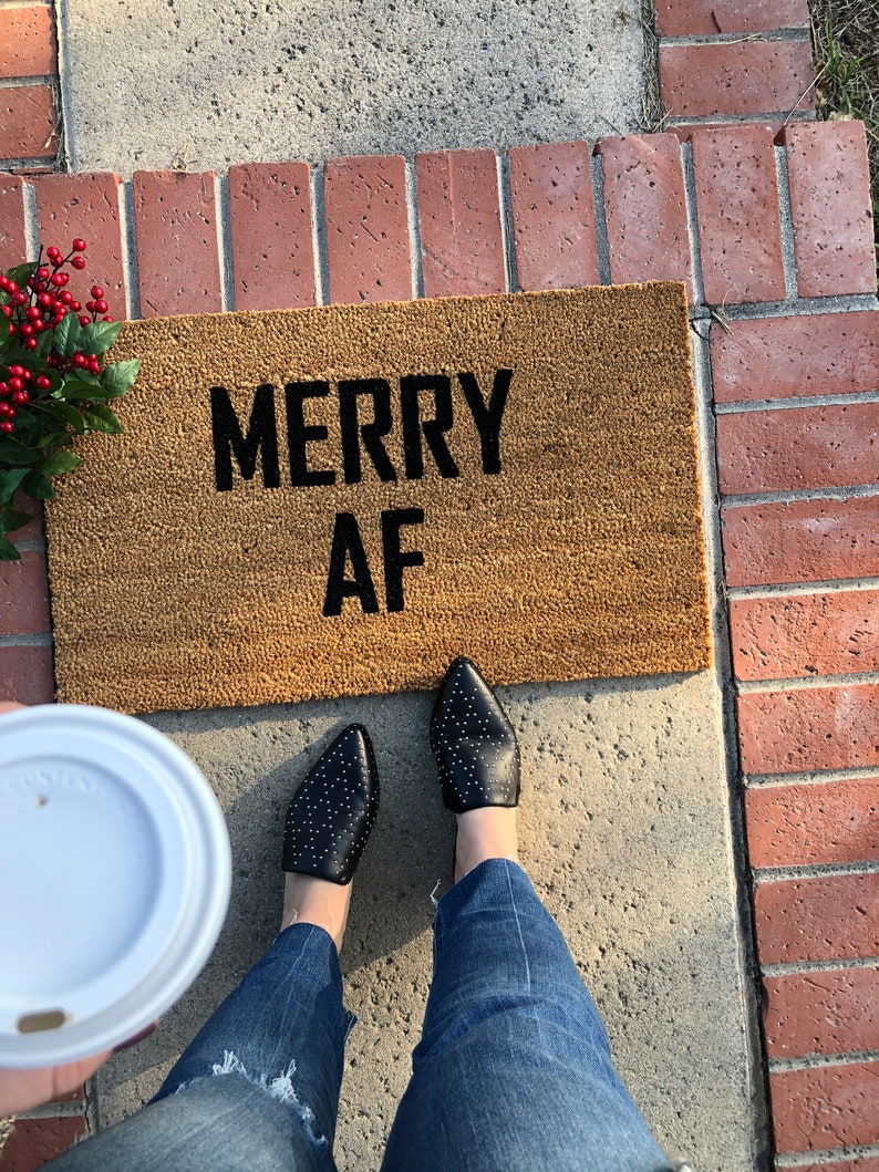 May include: A brown doormat with the text "Merry AF" in black lettering.