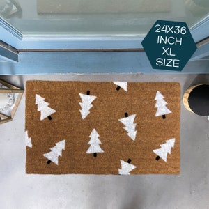 May include: A brown coir doormat with a white Christmas tree pattern. The doormat is 24 inches by 36 inches and is labeled "XL Size".