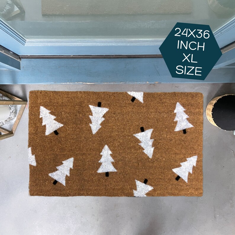May include: A brown coir doormat with a white Christmas tree pattern. The doormat is 24 inches by 36 inches and is labeled "XL Size".