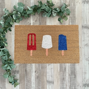 May include: A brown doormat with three popsicle designs. The popsicles are red, white, and blue.