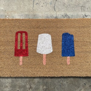 May include: A brown coir doormat with three popsicle designs. The popsicles are red, white, and blue.