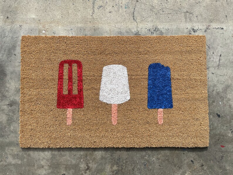 May include: A brown coir doormat with three popsicle designs. The popsicles are red, white, and blue.