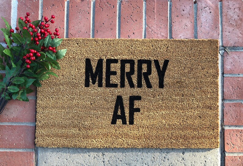 May include: A brown coir doormat with the text "MERRY AF" in black lettering.