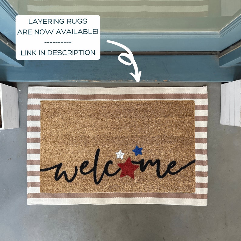 May include: A brown welcome mat with white and brown stripes. The mat has the word "welcome" written in black cursive with three stars in the center. The stars are red, white, and blue.