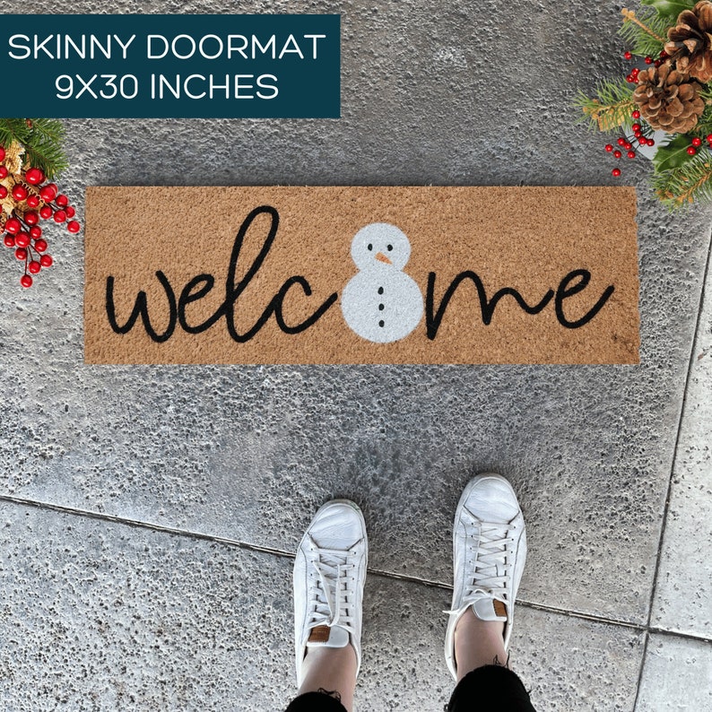 May include: A brown coir doormat with the word "welcome" in black script and a white snowman in the center. The doormat is 9x30 inches.