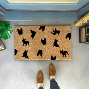 K&ouml;nnte beinhalten: Eine braune Kokosmatte mit schwarzen Silhouetten von franz&ouml;sischen Bulldoggen in verschiedenen Posen.
