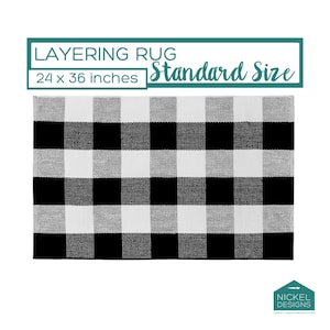 May include: A rectangular layering rug featuring a black and white buffalo check pattern. The text above reads LAYERING RUG Standard Size 24 x 36 inches. A logo in the bottom right corner displays the text NICKEL DESIGNS custom + craft welcome mats.