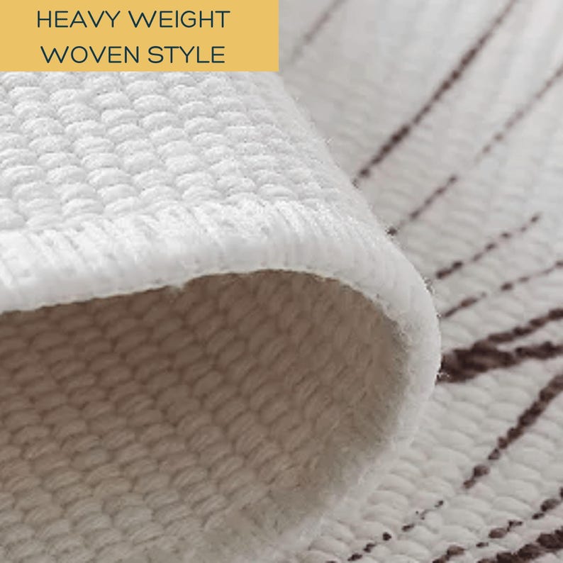 May include: A white fabric textile with a textured, heavy weight woven style. The material is folded over to reveal a thick, layered edge. A subtle, dark brown linear pattern is visible on the flat portion of the fabric surface.