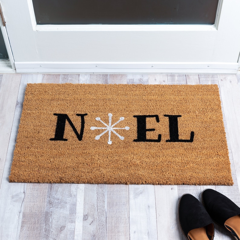 May include: A brown coir doormat with the word "NOEL" in black letters and a white snowflake in the center.