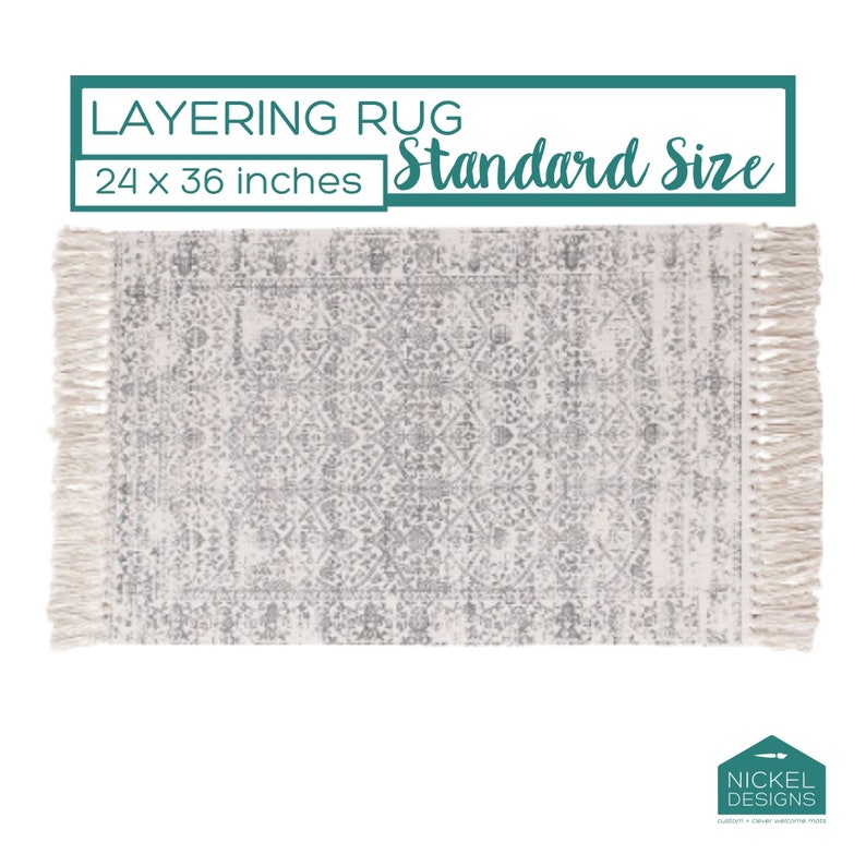 May include: A white and gray patterned rug with fringe on the edges. The rug is 24 x 36 inches and is labeled "Layering Rug Standard Size".