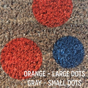 May include: A brown doormat with large orange and blue dots. The text "ORANGE - LARGE DOTS GRAY - SMALL DOTS" is printed on the doormat.