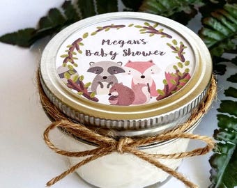 May include: A small glass jar with a white label that says "Megan's Baby Shower" and features a raccoon, fox, and squirrel. The jar is tied with twine and has a silver lid.