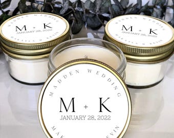 May include: Three small glass jar candles with gold-colored lids. Each lid has a white label with the text "MADDEN WEDDING" and the initials "M + K" with the date "JANUARY 28, 2022" and names "MAKAYLA & KEVIN".