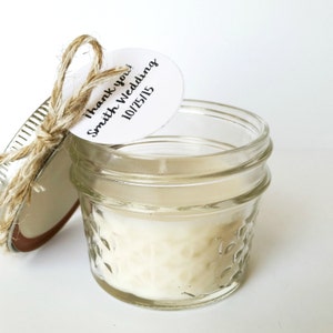 May include: A small glass jar candle with a white lid and a twine bow. A white tag with black text reads "Thank you! Smith Wedding 10/25/15".