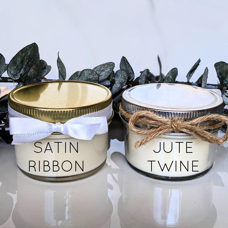 May include: Two small glass candle jars with white lids. The jar on the left is decorated with a white satin ribbon and the text "SATIN RIBBON". The jar on the right is decorated with brown jute twine and the text "JUTE TWINE".