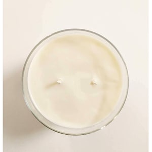 May include: A clear glass jar candle with a white wax top and two wicks.