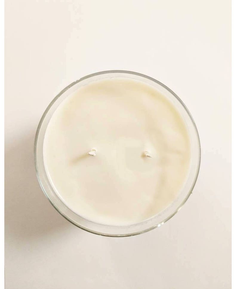 May include: A clear glass jar candle with a white wax top and two wicks.