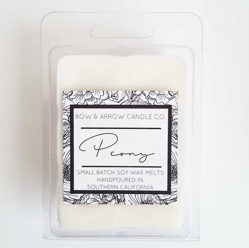 May include: A white soy wax melt in a clear plastic container with a black and white label that reads "BOW & ARROW CANDLE CO. Peony SMALL BATCH SOY WAX MELTS HANDPOURED IN SOUTHERN CALIFORNIA"