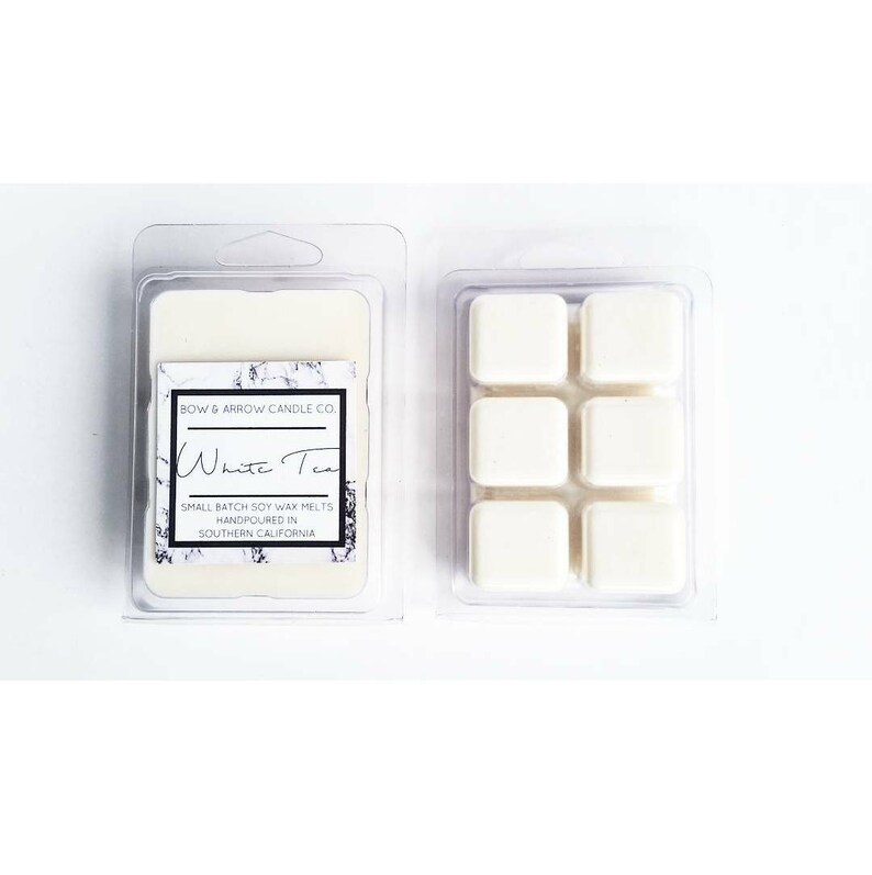 Puede incluir: Seis cubos de cera de soja blanca en un recipiente de pl&aacute;stico transparente. La etiqueta dice "BOW & ARROW CANDLE CO. White Tea SMALL BATCH SOY WAX MELTS HANDPOURED IN SOUTHERN CALIFORNIA."