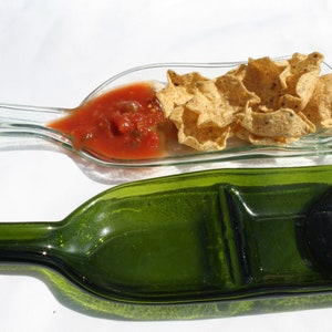 May include: Two glass serving dishes made from recycled wine bottles. The top dish is clear glass and holds tortilla chips and salsa. The bottom dish is green glass and has two sections.