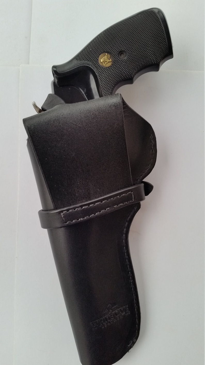 May include: Black leather holster with a stitched strap and the text "Triple C Leather" embossed on the bottom. A black handgun is partially visible inside the holster.