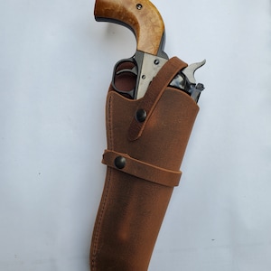 May include: A brown leather holster with a black revolver inside. The holster has a strap with a snap closure.