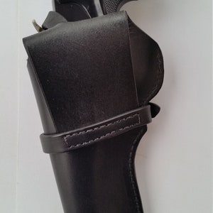 May include: A black revolver pistol with a textured grip is partially inserted into a black leather holster. The holster has a strap and the words "WHITE OAK LEATHER" are visible on the front.