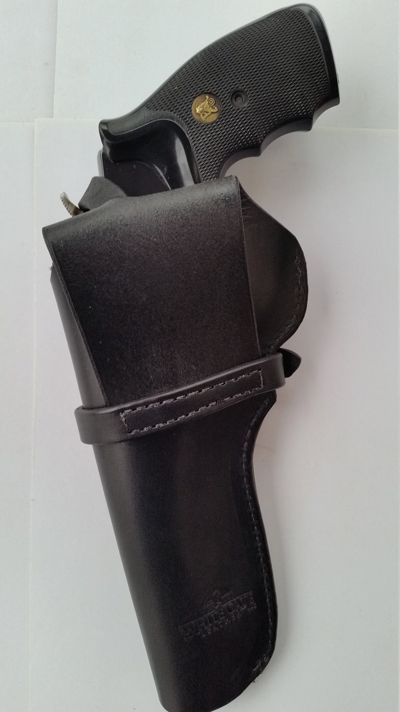 May include: A black revolver pistol with a textured grip is partially inserted into a black leather holster. The holster has a strap and the words "WHITE OAK LEATHER" are visible on the front.