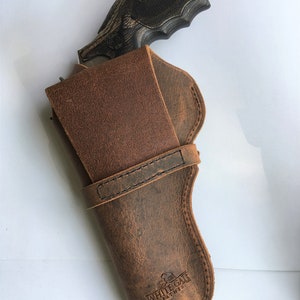 May include: A brown leather holster with a revolver. The holster has a distressed finish and the text "WHITE GATE LEATHER" is visible. The revolver has a black grip and a silver barrel.