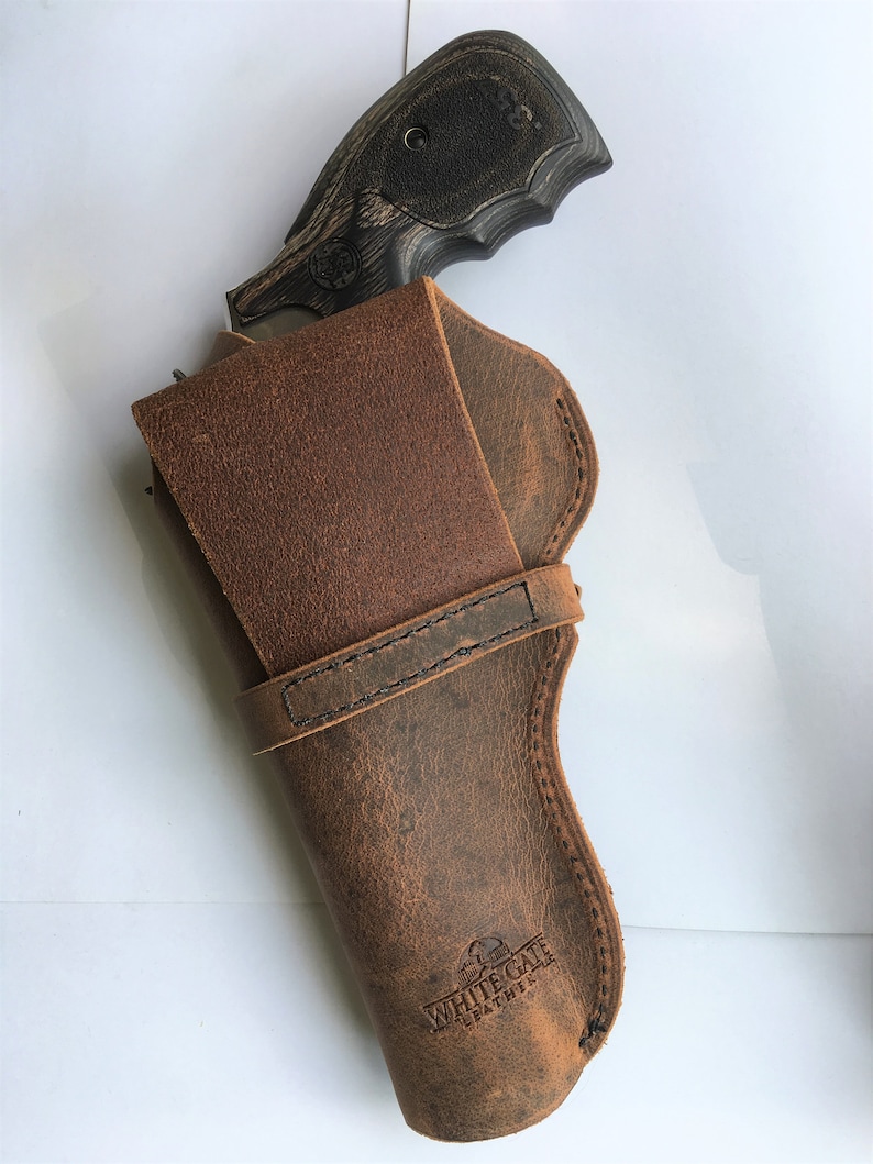 May include: A brown leather holster with a revolver. The holster has a distressed finish and the text "WHITE GATE LEATHER" is visible. The revolver has a black grip and a silver barrel.