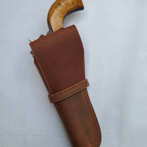 May include: A brown leather holster with a stitched strap and the text "Whitetail Leather" on the side. A wooden-handled revolver is partially visible inside the holster.