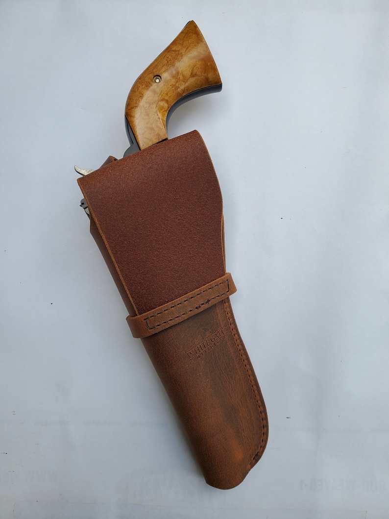 May include: A brown leather holster with a stitched strap and the text "Whitetail Leather" on the side. A wooden-handled revolver is partially visible inside the holster.