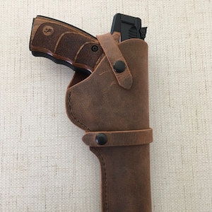 May include: A brown leather holster with a black snap closure and a black gun inside.