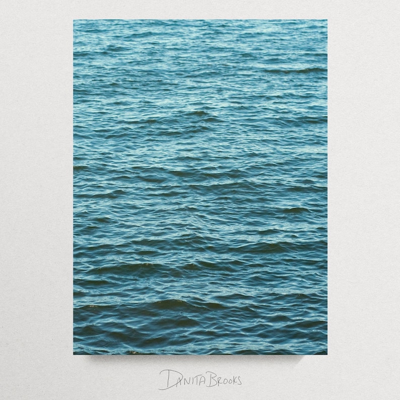 Op de afbeelding: Een rechthoekige print met een close-up van kabbelend water in tinten blauw en blauwgroen. Het wateroppervlak is getextureerd met kleine golven, waardoor een gevoel van diepte en beweging ontstaat. De handtekening van de kunstenaar, "DANITA BROOKS", staat onderaan.