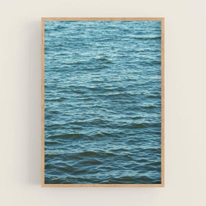 Op de afbeelding: Een ingelijste print met een close-up van oceaanwater. Het water heeft een mix van blauwe en teal tinten, met zachte golven die een textuur cre&euml;ren. De houten lijst voegt een natuurlijke touch toe aan het kunstwerk.