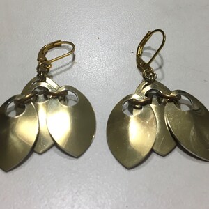 May include: A pair of gold-toned earrings with three teardrop-shaped charms on each earring.