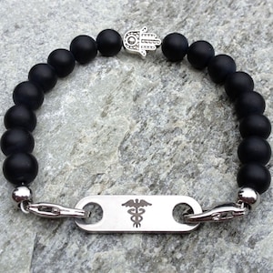 May include: Black beaded bracelet with a silver hamsa charm and a medical alert tag with a caduceus symbol.