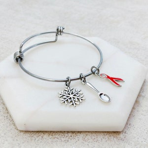 May include: A silver bangle bracelet with three charms: a snowflake, a spoon, and a red ribbon.