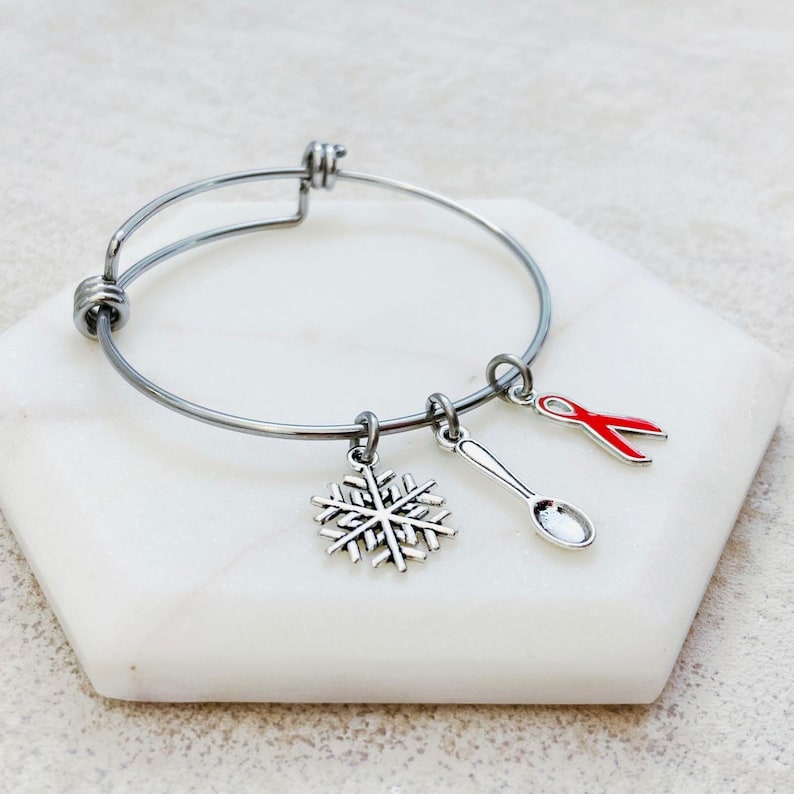 May include: A silver bangle bracelet with three charms: a snowflake, a spoon, and a red ribbon.
