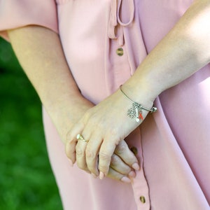 May include: A silver charm bracelet with a snowflake, a spoon, and a red ribbon charm. The bracelet is on a woman's wrist.