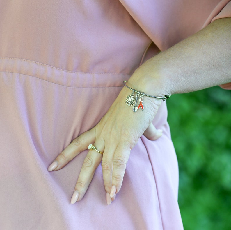 May include: A silver charm bracelet with a snowflake, a bell, and a red ribbon charm. The bracelet is on a person's wrist.