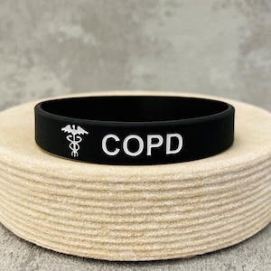 May include: Black silicone medical alert bracelet with a white medical symbol and the text "COPD".