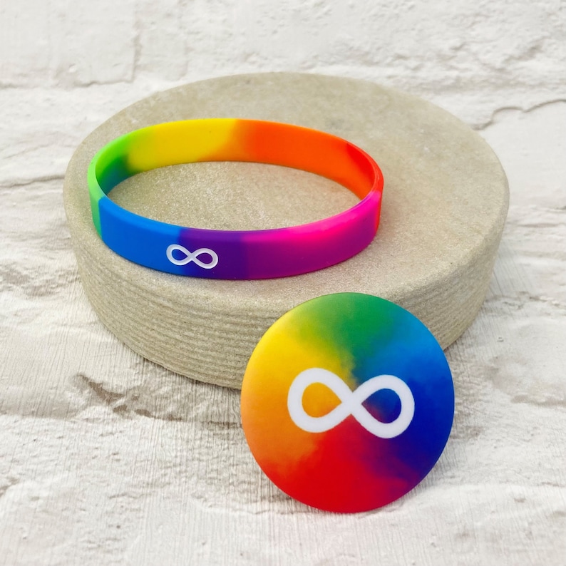 K&ouml;nnte beinhalten: Ein Regenbogen-Silikonarmband mit einem wei&szlig;en Unendlichkeitszeichen. Ein runder Aufkleber mit einem passenden Regenbogen-Unendlichkeitszeichen.