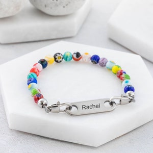 May include: A colorful beaded bracelet with a silver nameplate engraved with the name "Rachel".