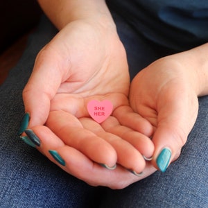 Hand holding pronoun pin to show size comparison and scale
