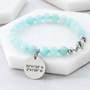 May include: A light blue beaded bracelet with a silver charm that has the coordinates 52°41'22" N 2°01'55" W engraved on it.