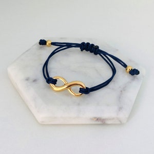 Op de afbeelding: Een verstelbare armband van donkerblauwe koord met een gouden oneindigheidssymbool bedel.