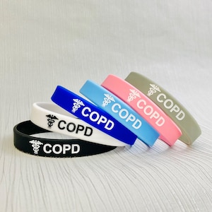 May include: Five silicone wristbands in different colours: black, white, blue, light blue, and pink. Each wristband has a white medical symbol and the word "COPD" printed on it.