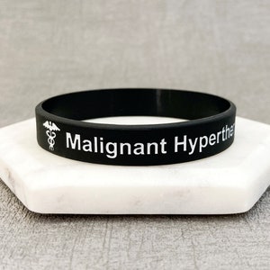 Op de afbeelding: Zwart siliconen armband met witte tekst "Malign hyperthermie" en een wit medisch symbool.