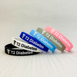 May include: Five silicone wristbands in different colors: black, white, blue, light blue, and pink. Each band has a white medical symbol and the text "T2 Diabetes".